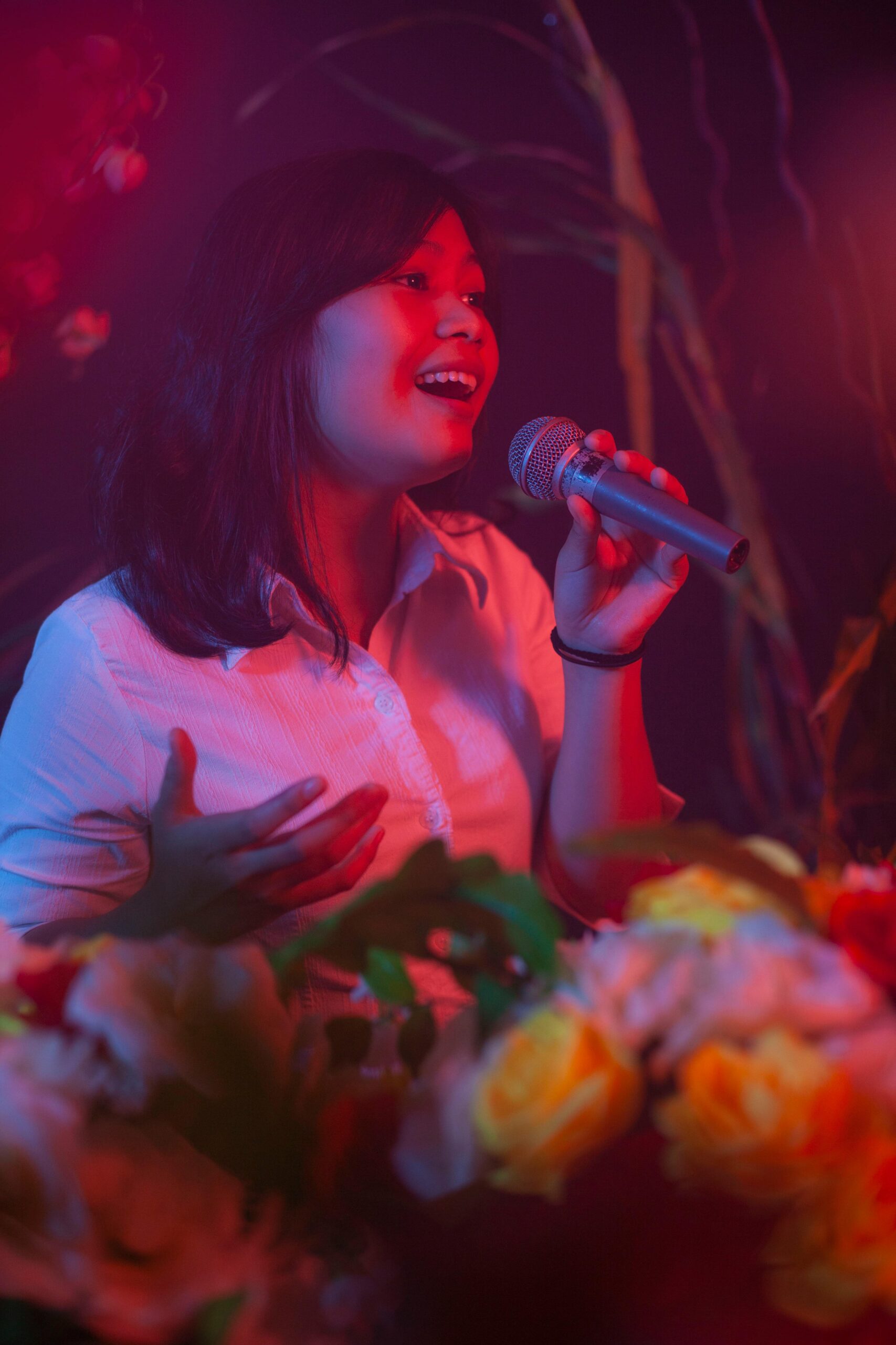 A vibrant portrait of an Asian woman singing into a microphone surrounded by flowers.